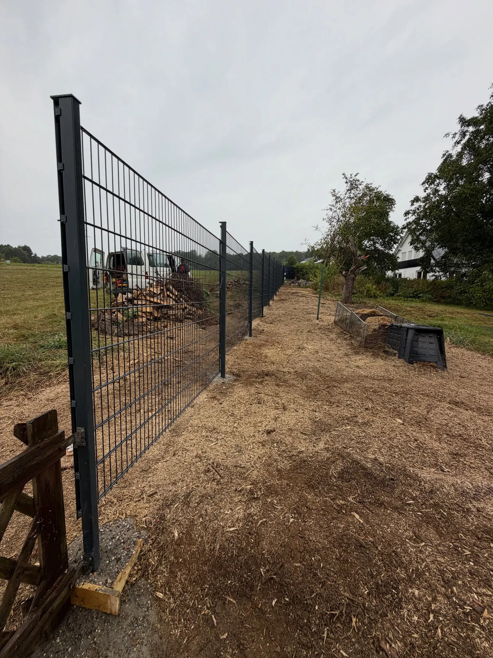 Dunkler Doppelstabmattenzaun entlang einer freigelegten Grundstücksgrenze mit Wiese im Hintergrund
