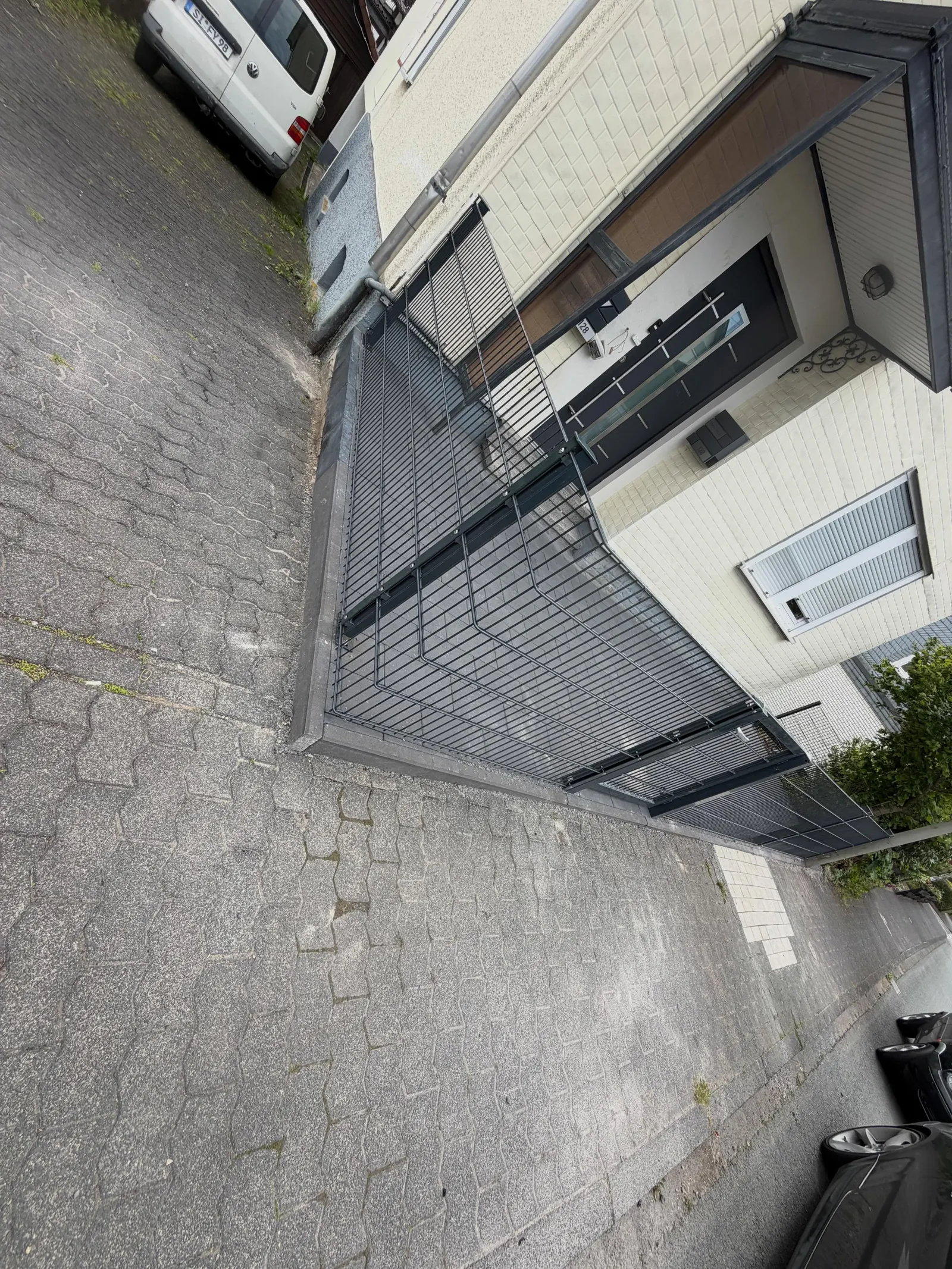 Neu gepflasterter Hauseingang mit anthrazitfarbenem Zaun und Tor vor einem hellen Haus