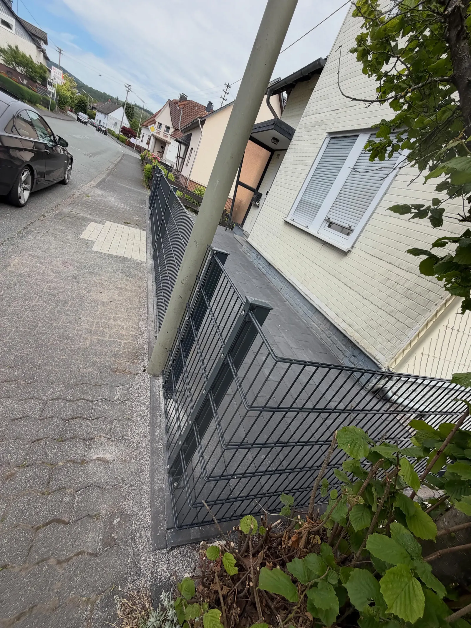 Dunkler Zaun mit Gartentor entlang des gepflasterten Hauseingangs