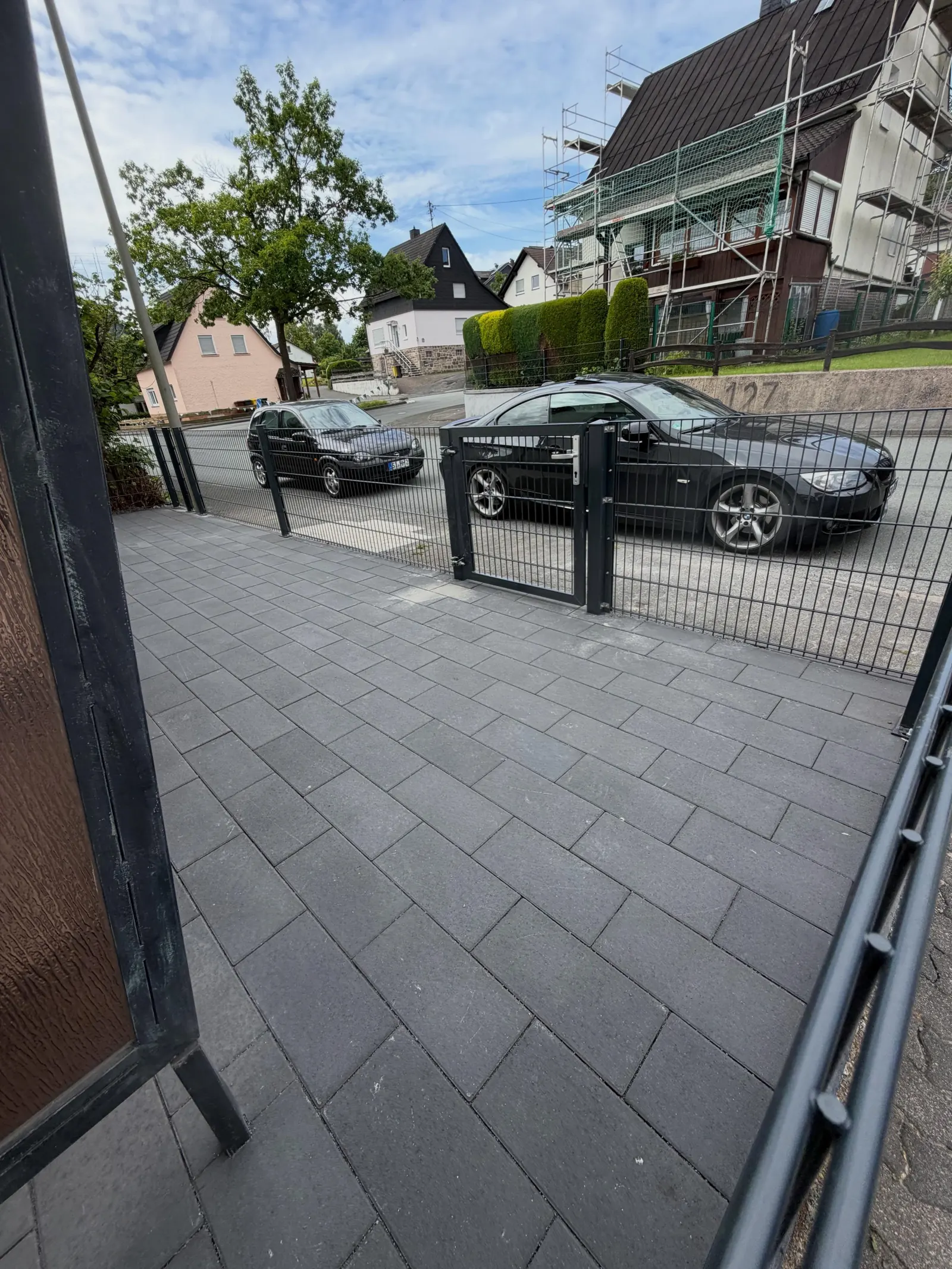 Blick über dunkelgraues Pflaster zum Gartentor und zum Gehweg