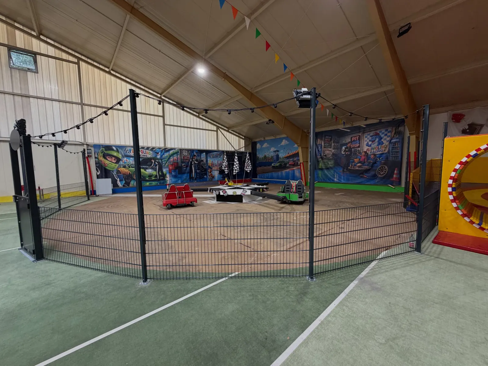 Zaunelemente entlang der Spielfläche mit kleinen Fahrzeugen in einer Halle