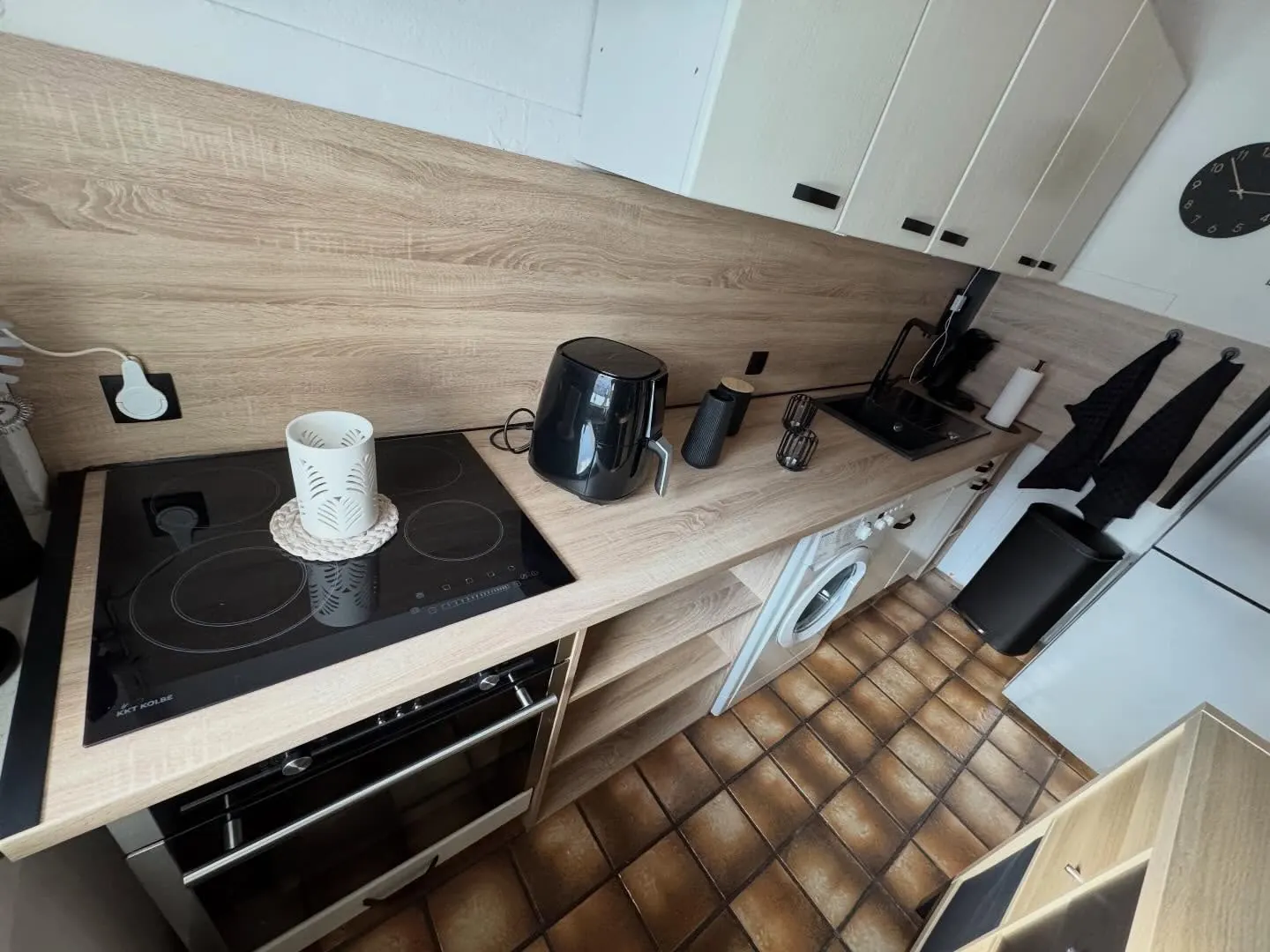 Seitlicher Blick auf die helle Küche mit Arbeitsplatte, Regalen und Spritzschutz in Holzoptik