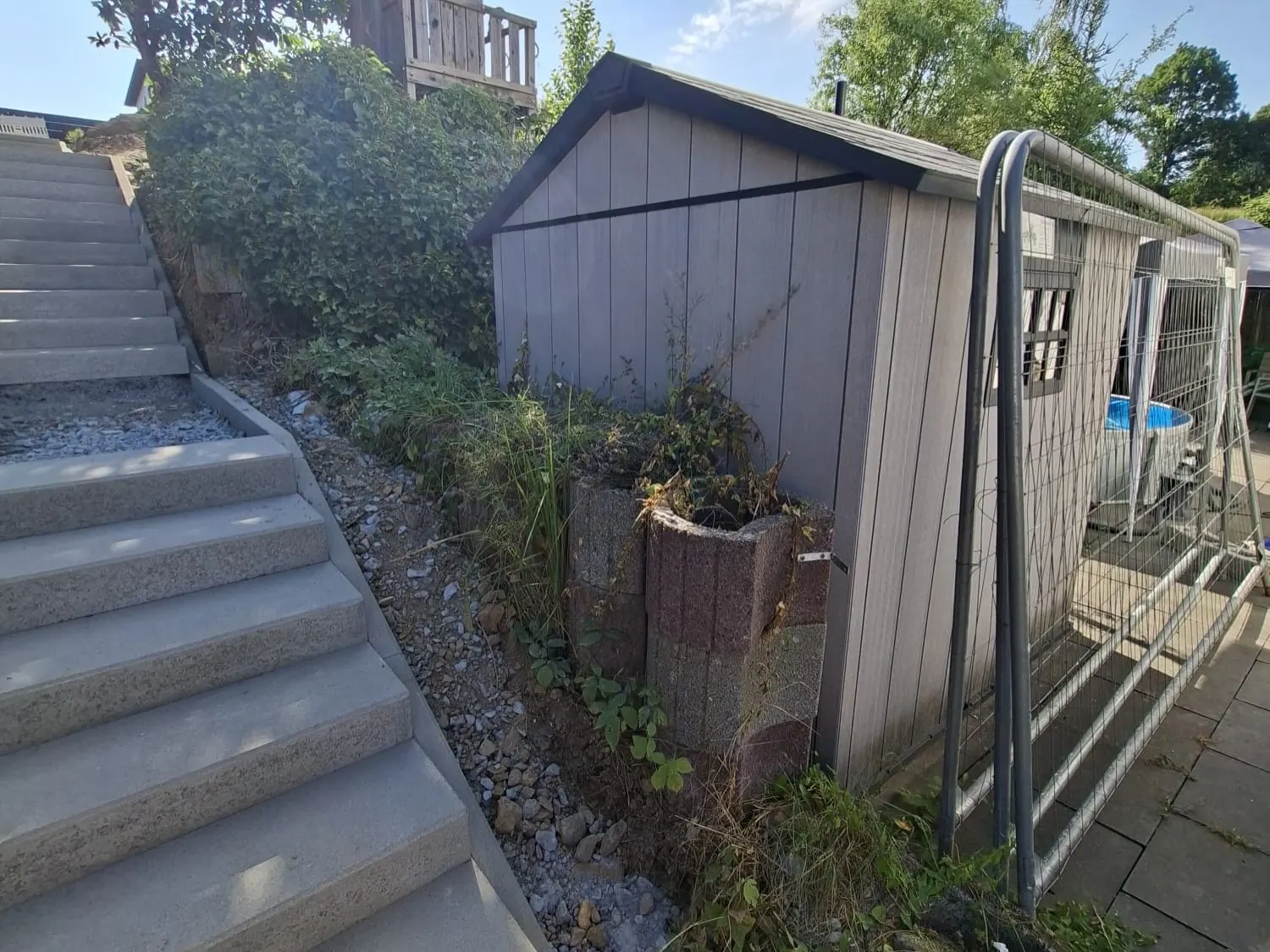 Provisorischer Bauzaun neben einer Außentreppe mit Schotterpodest und Gartenhaus