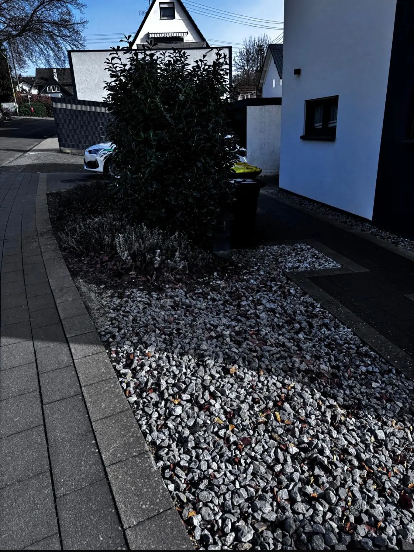 Seitliche Ansicht des Vorgartens vor der Umgestaltung mit Strauch und hellen Steinen